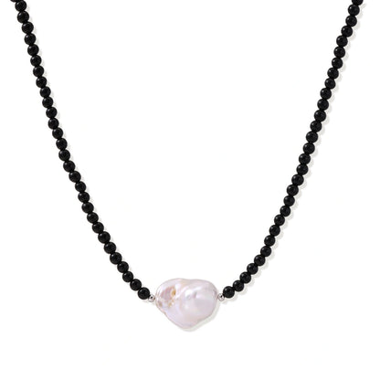 Beaded black agate necklace with iridescent baroque freshwater pearl centerpiece on cream background.