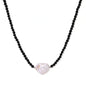 Beaded black agate necklace with iridescent baroque freshwater pearl centerpiece on cream background.