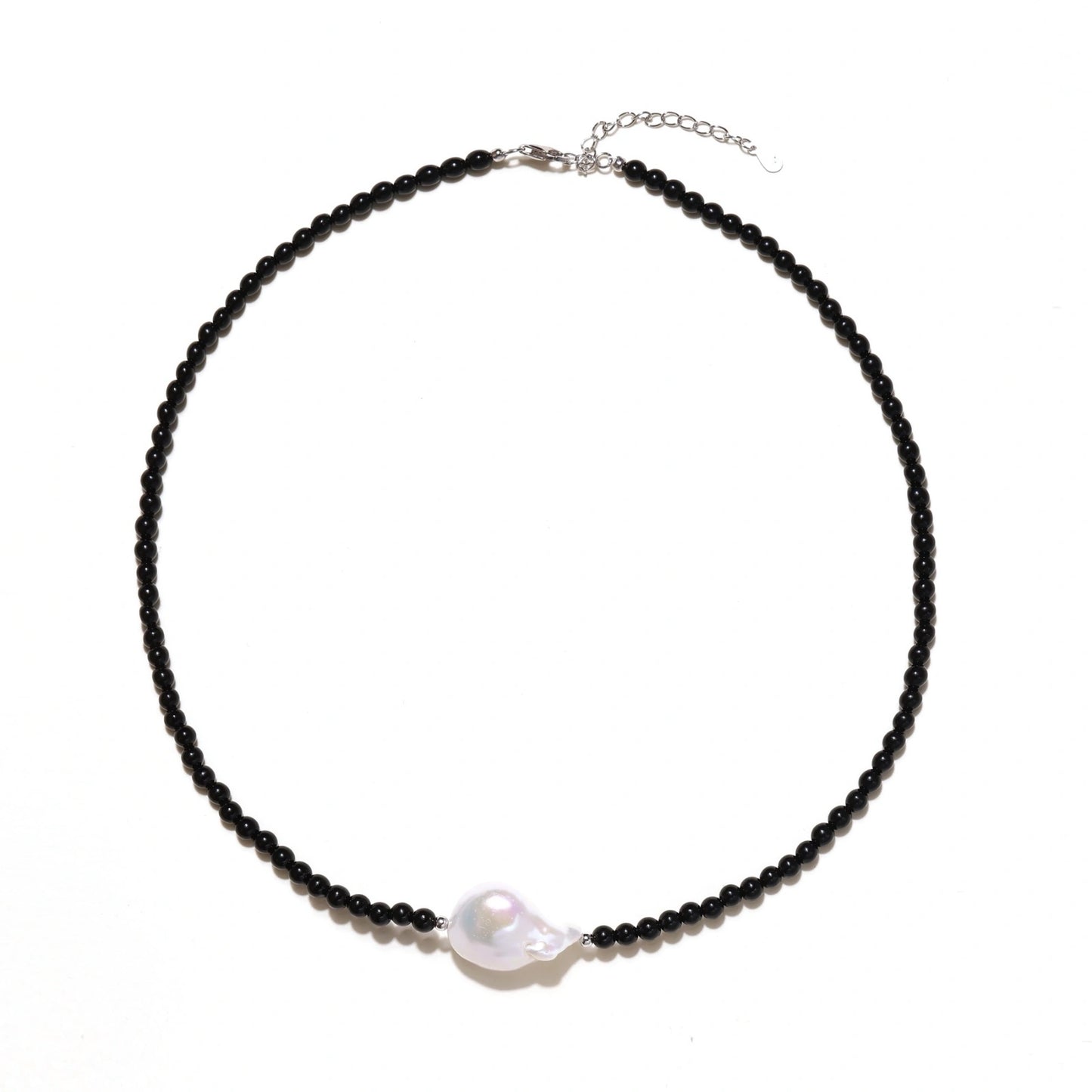 Beaded black agate necklace with iridescent baroque freshwater pearl centerpiece on cream background.