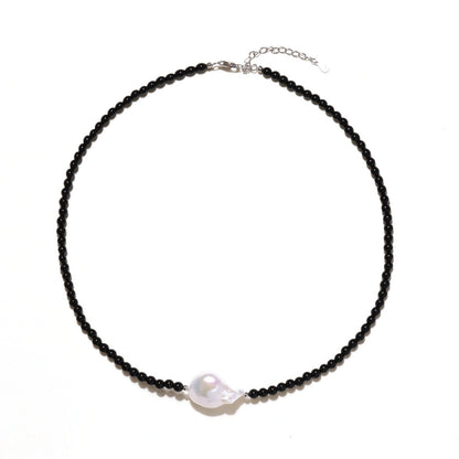 Beaded black agate necklace with iridescent baroque freshwater pearl centerpiece on cream background.
