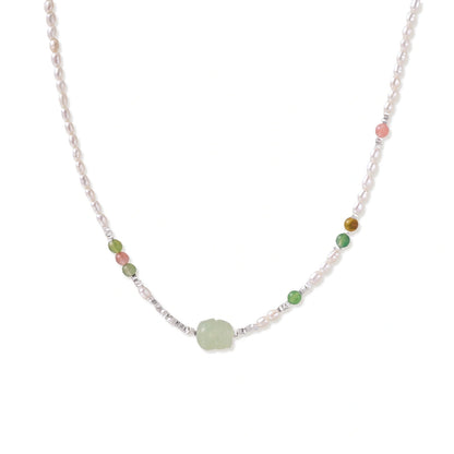Delicate pearl necklace with pale green serpentine jade centerpiece and colorful agate beads on cream background