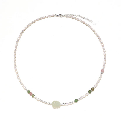 Delicate pearl necklace with pale green serpentine jade centerpiece and colorful agate beads on cream background