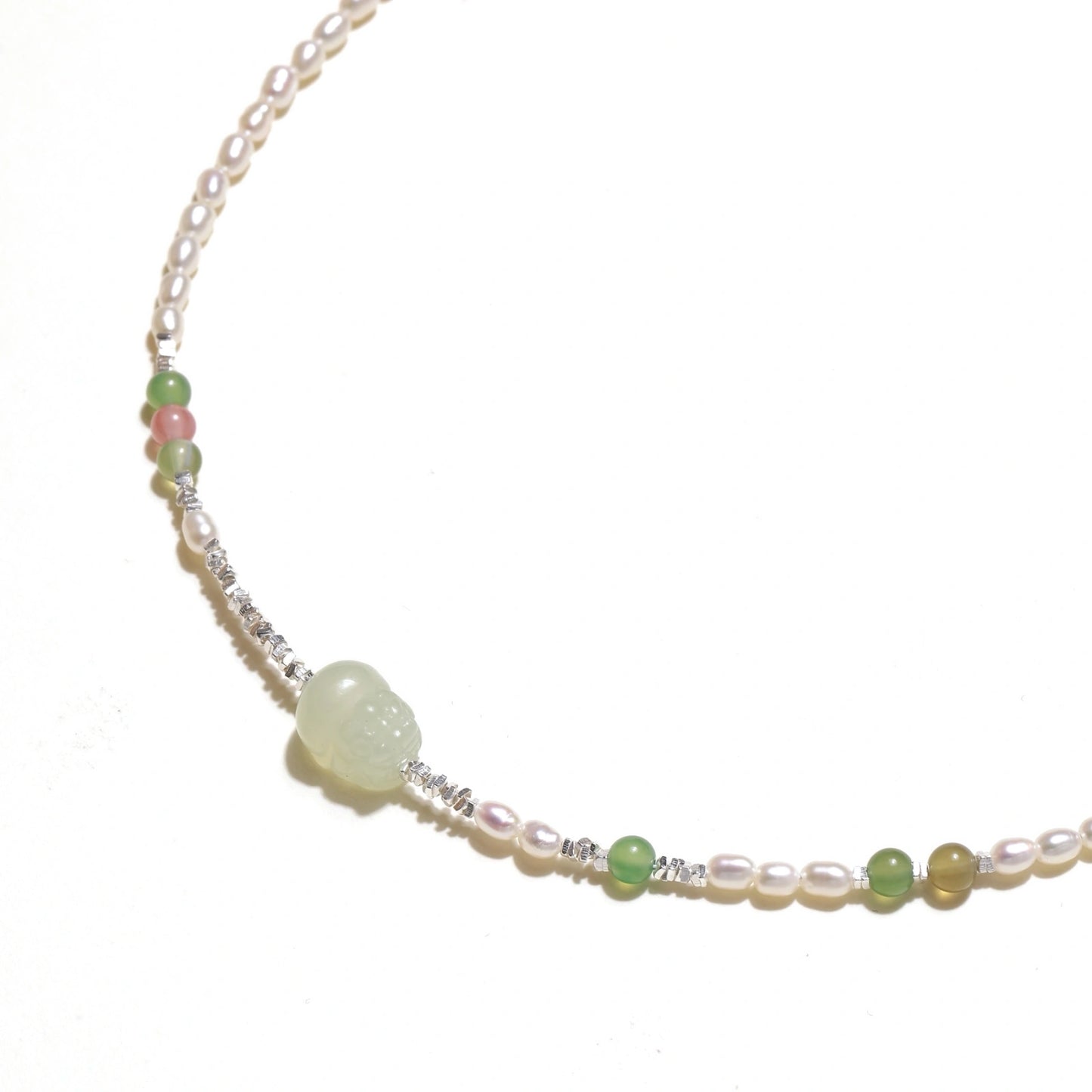 Delicate pearl necklace with pale green serpentine jade centerpiece and colorful agate beads on cream background