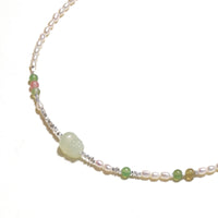 Delicate pearl necklace with pale green serpentine jade centerpiece and colorful agate beads on cream background