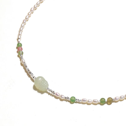 Delicate pearl necklace with pale green serpentine jade centerpiece and colorful agate beads on cream background
